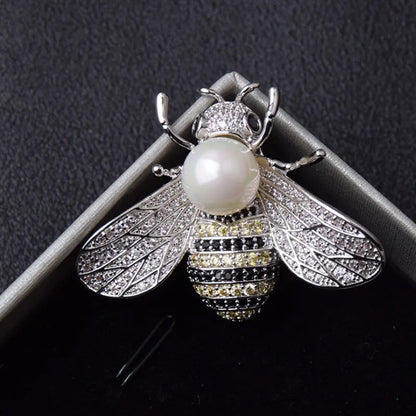 Silver bee-shaped brooch with a pearl body on a dark background