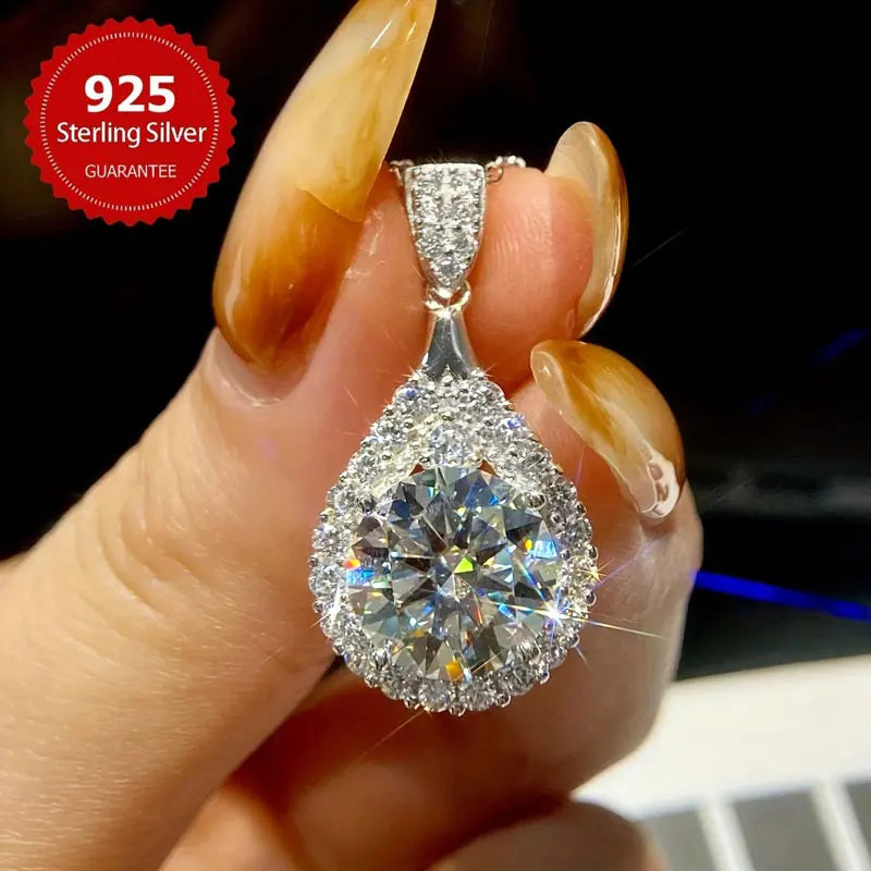 Teardrop-shaped silver pendant with clear gemstone held by a hand, 925 Sterling Silver label visible.