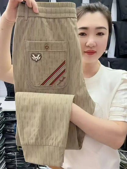 Woman holding beige pants with a brand logo, standing in a clothing store.