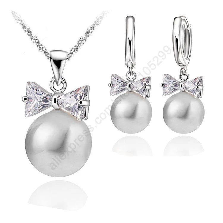 Pearl necklace and earrings with bow accents on a white background