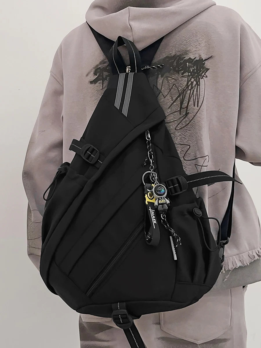Person wearing a black sling bag with a keychain on a plain background