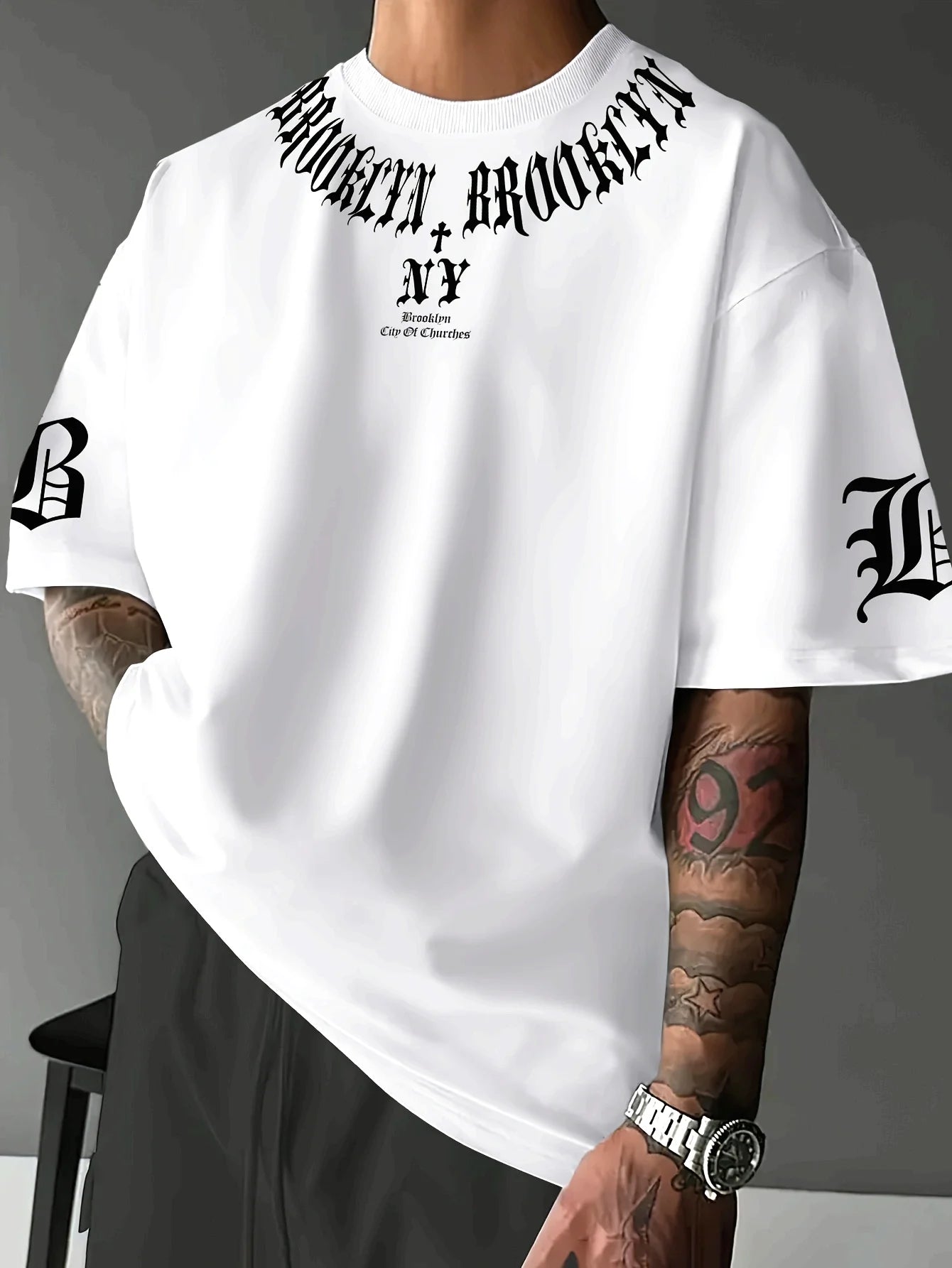 Person wearing a white t-shirt with 'Brooklyn, New York' text and tattoos on arms.