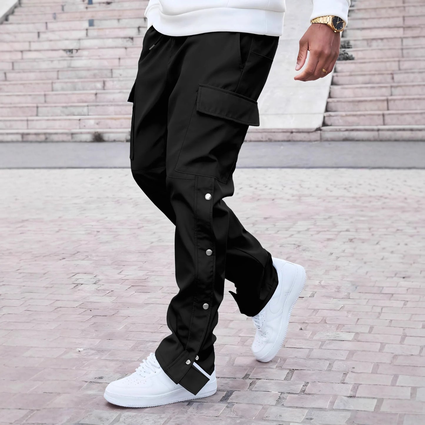 Person wearing black cargo pants and white sneakers on a brick pavement.