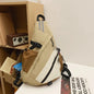 Beige and brown sling bag with black straps on a white surface.