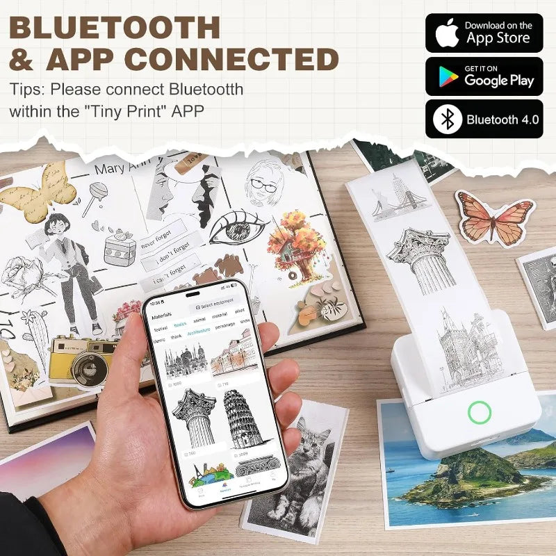 Hand holding a smartphone with an app displaying printed designs, next to a Tiny Print device and printed cards on a wooden surface.