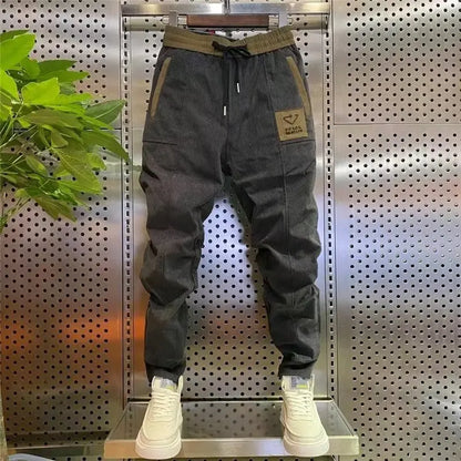 Gray jogger pants with a brand logo on a metallic stand against a perforated metal wall.
