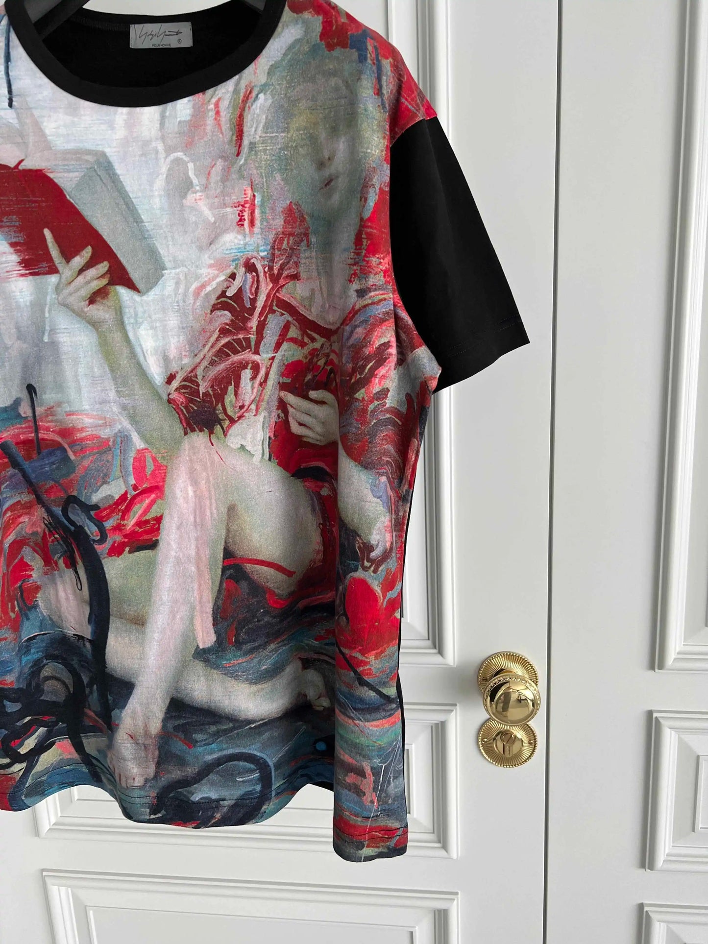 T-shirt with artistic design of a nude figure holding a book against a white door.