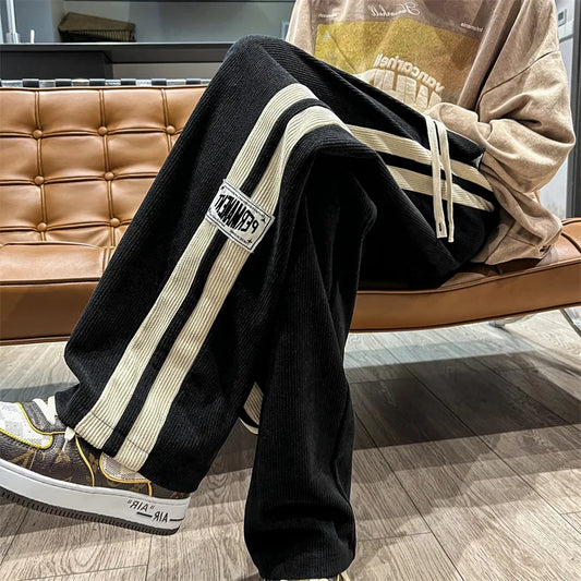 Person wearing black pants with white stripes sitting on a brown leather couch.