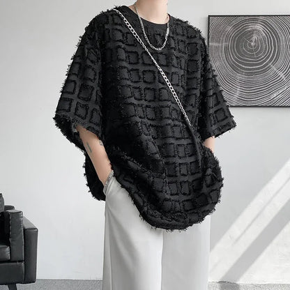 Person wearing a black textured poncho in a minimalistic room.