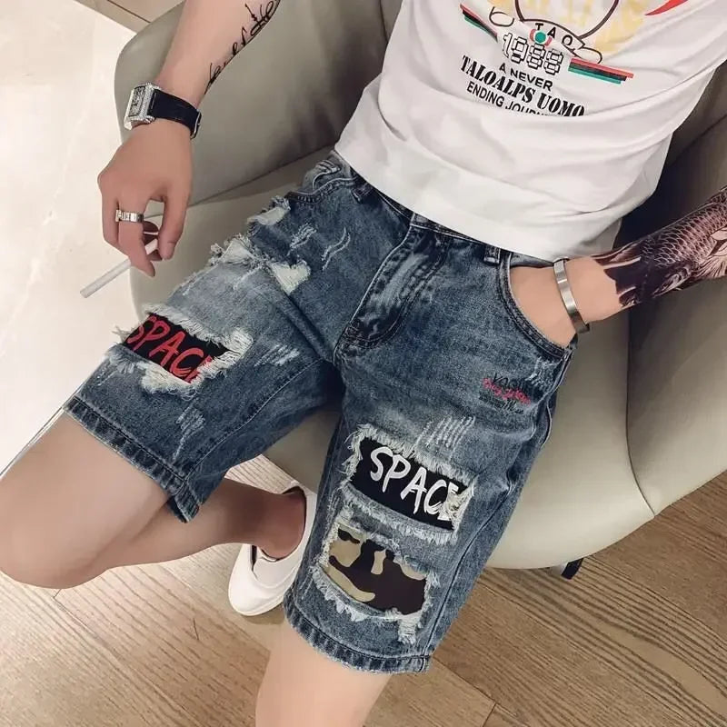 Person wearing ripped denim shorts with patches sitting on a chair.