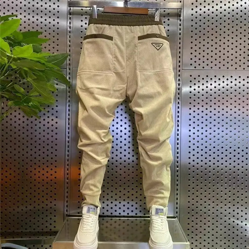 Beige jogger pants with brown accents on a hanger against a metallic wall.