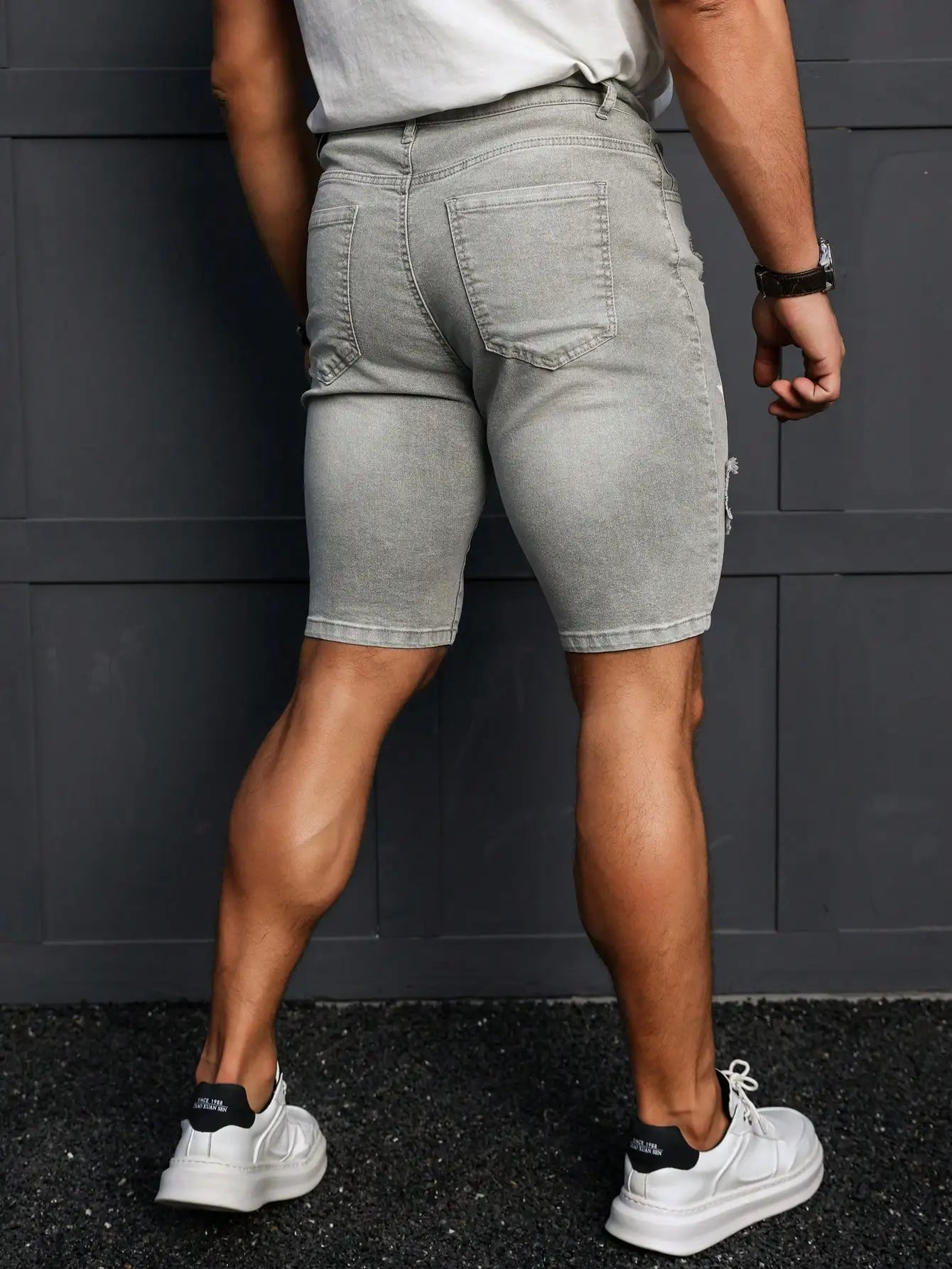 Person wearing gray shorts and white sneakers against a dark background