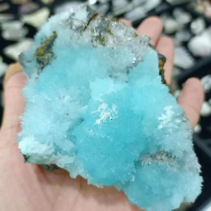 Turquoise crystal held in a hand with a blurred natural background