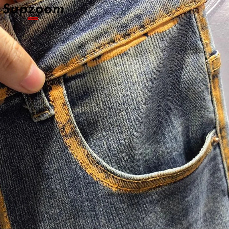 Close-up of a person holding up a blue denim pocket with yellow stitching.