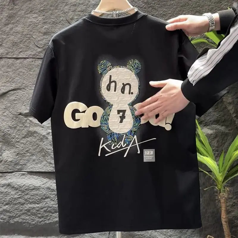 Black t-shirt with graphic design and text held by a person against a stone wall.