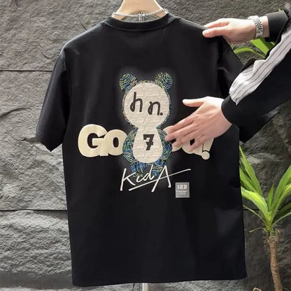Black t-shirt with graphic design and text held by a person against a stone wall.