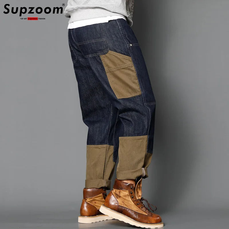 Person wearing patchwork jeans with brown and blue colors on a gray background, brand 'Supzoom' visible.