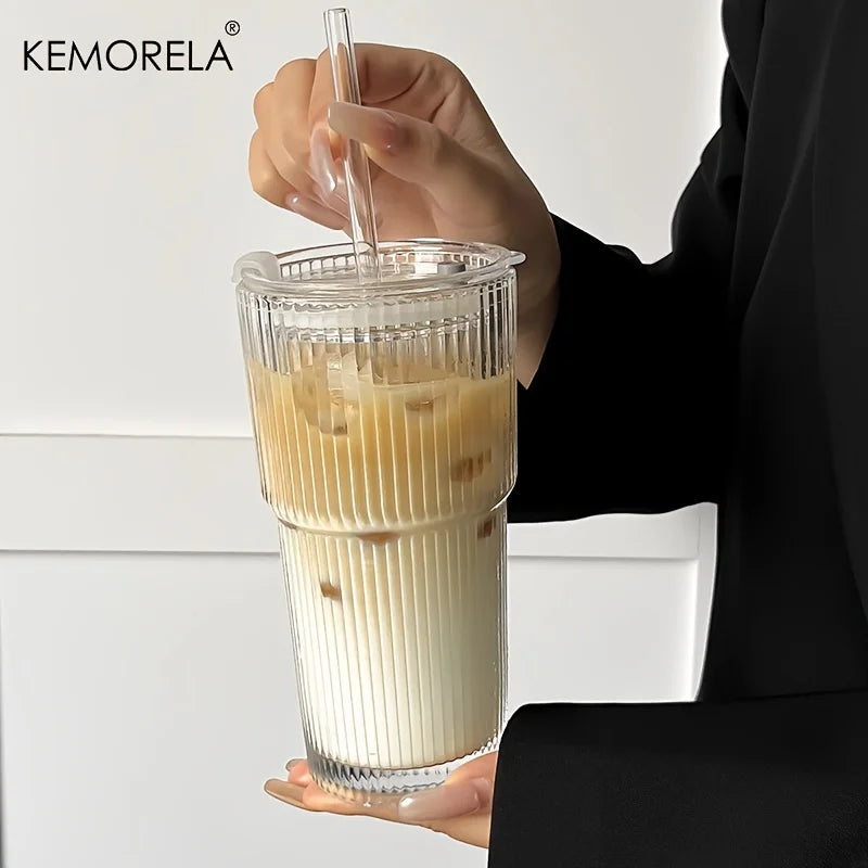 Person holding a clear plastic cup with layered drink and straw against a white background