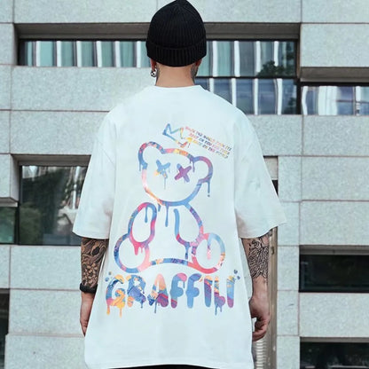 Person wearing a white t-shirt with colorful graphics and text, standing in front of a building.