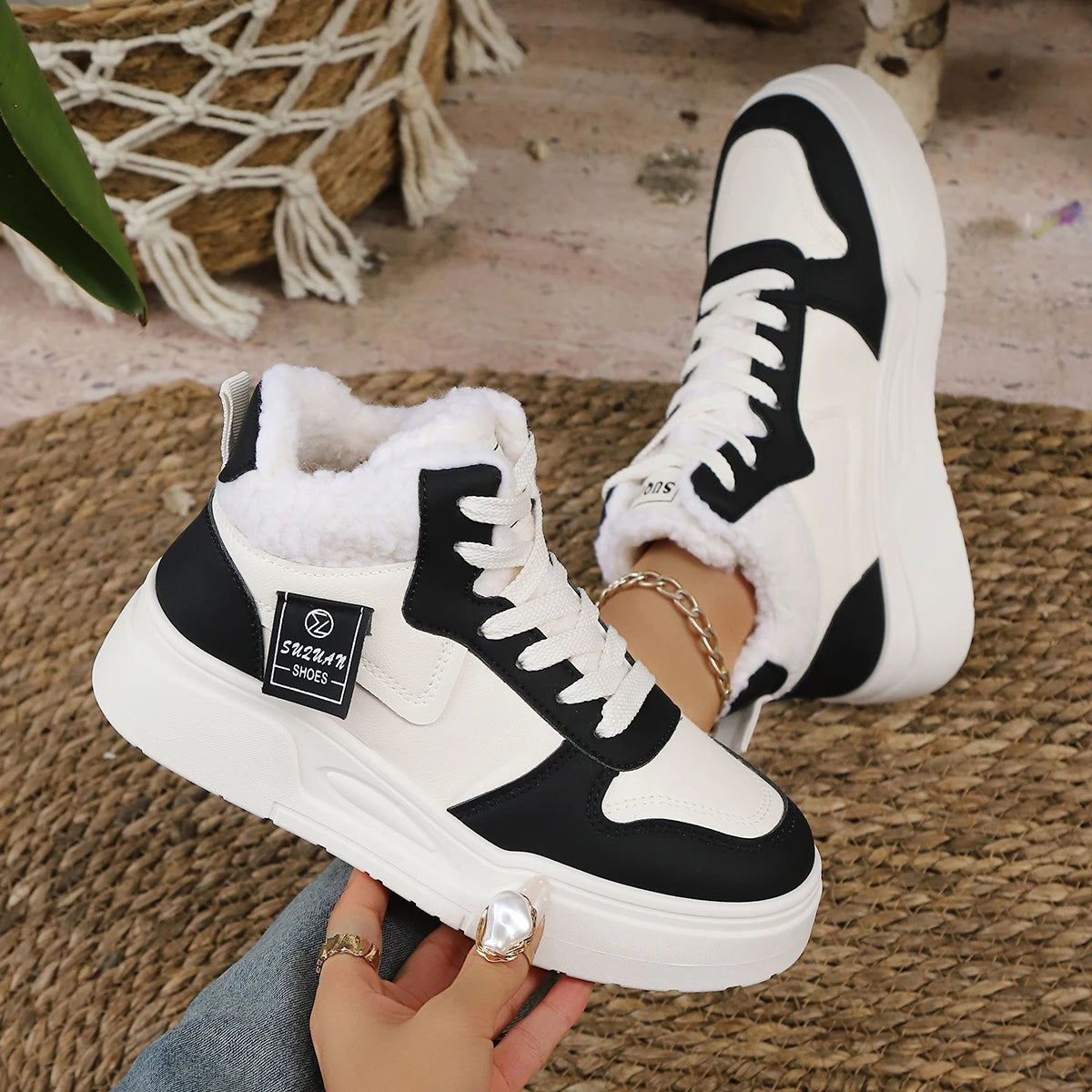 Black and white high-top sneakers with fur lining held by a person on a woven mat.
