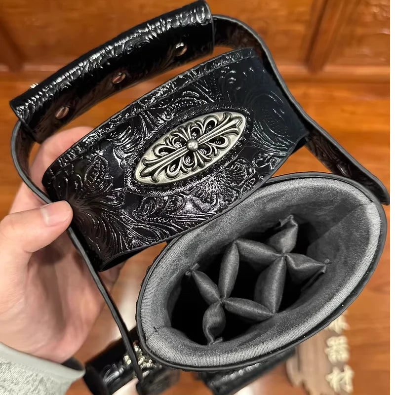 Black leather bag with intricate designs held by a hand on a wooden surface