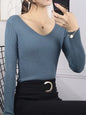 Woman wearing a blue ribbed sweater and black skirt, taking a mirror selfie.