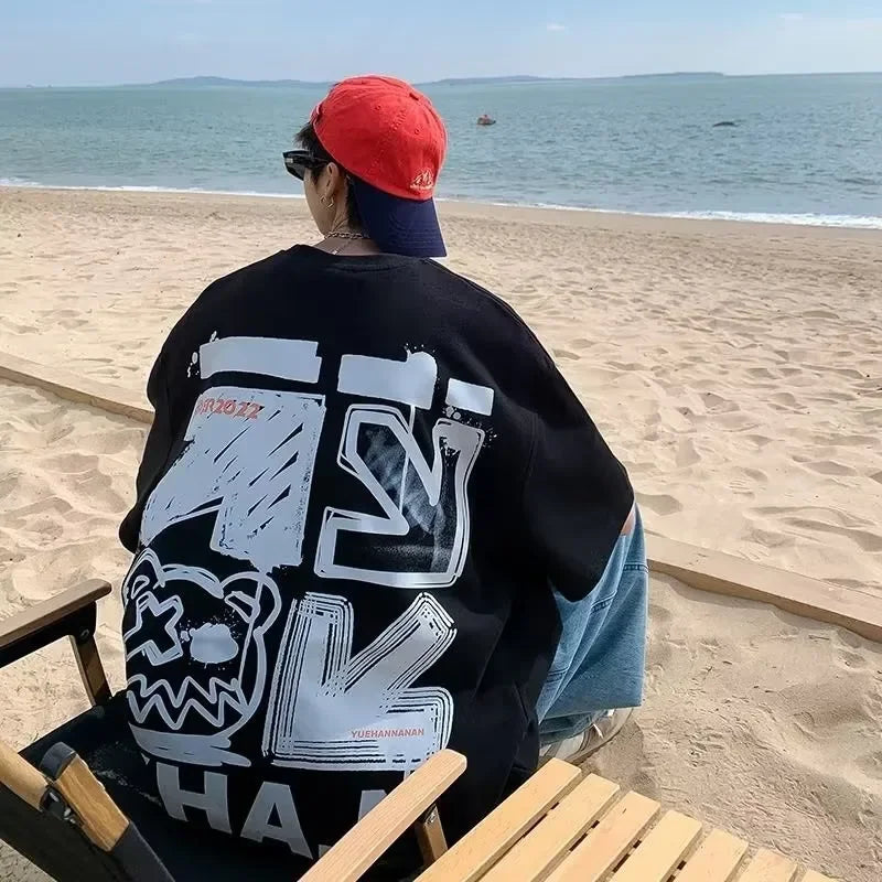 Person wearing a black sweatshirt with white graphics sitting on a beach.