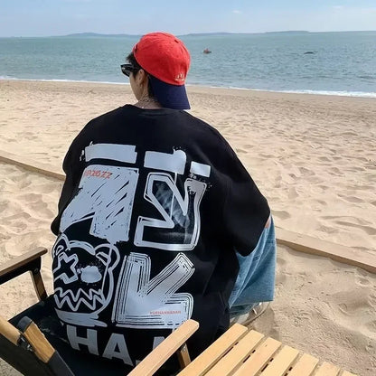 Person wearing a black sweatshirt with white graphics sitting on a beach.