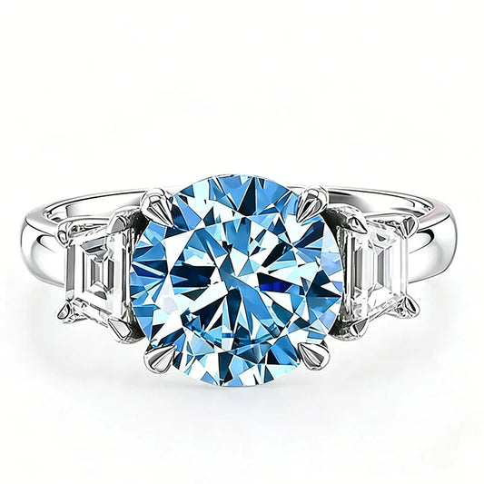 A silver three-stone ring featuring a large round brilliant-cut light blue center gemstone flanked by two baguette-cut side stones, set against a plain white background.