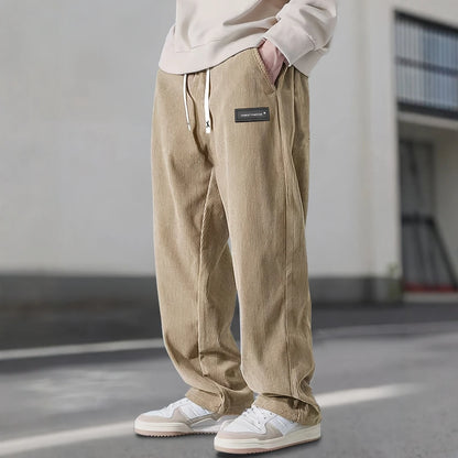 Person wearing beige corduroy pants with a brand logo, standing on a street.