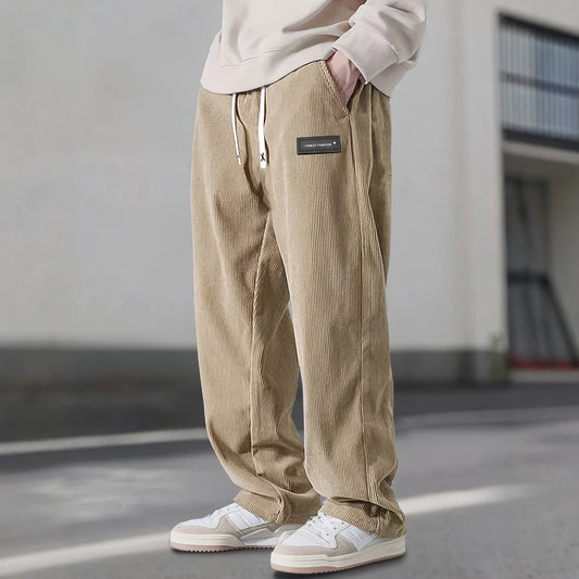 Person wearing beige corduroy pants with a brand logo, standing on a street.