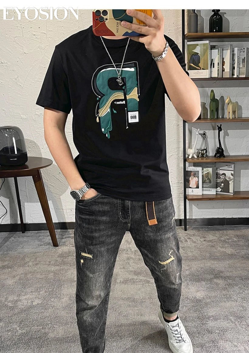Person wearing a black t-shirt with a colorful 'R' design and ripped jeans, standing in a room.