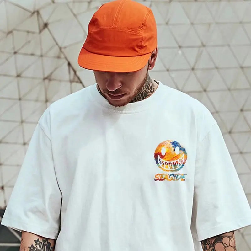 Person wearing a white t-shirt with a colorful logo and an orange cap against a geometric-patterned wall.