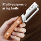 Hand holding a multi-purpose paring knife with wooden handle and metal blade on a brown background.