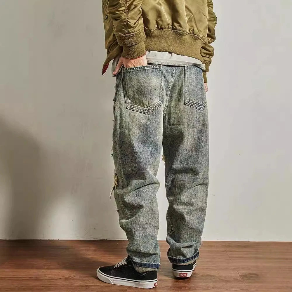Person wearing a green jacket and gray distressed jeans standing against a plain wall.