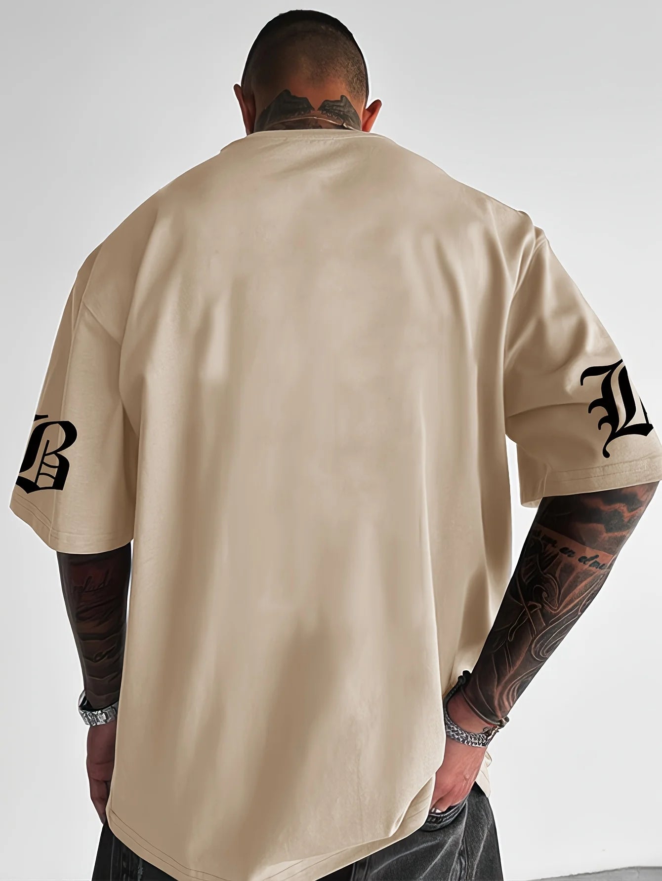 Man wearing a beige t-shirt with black logos on sleeves against a white background