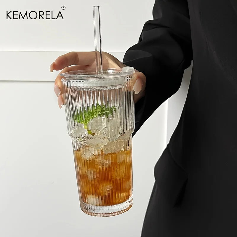Clear glass tumbler with a drink, straw, and ice cubes held by a person wearing a black outfit.