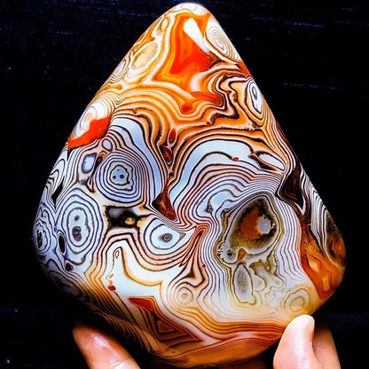 Marbled stone with intricate patterns held by a hand against a black background