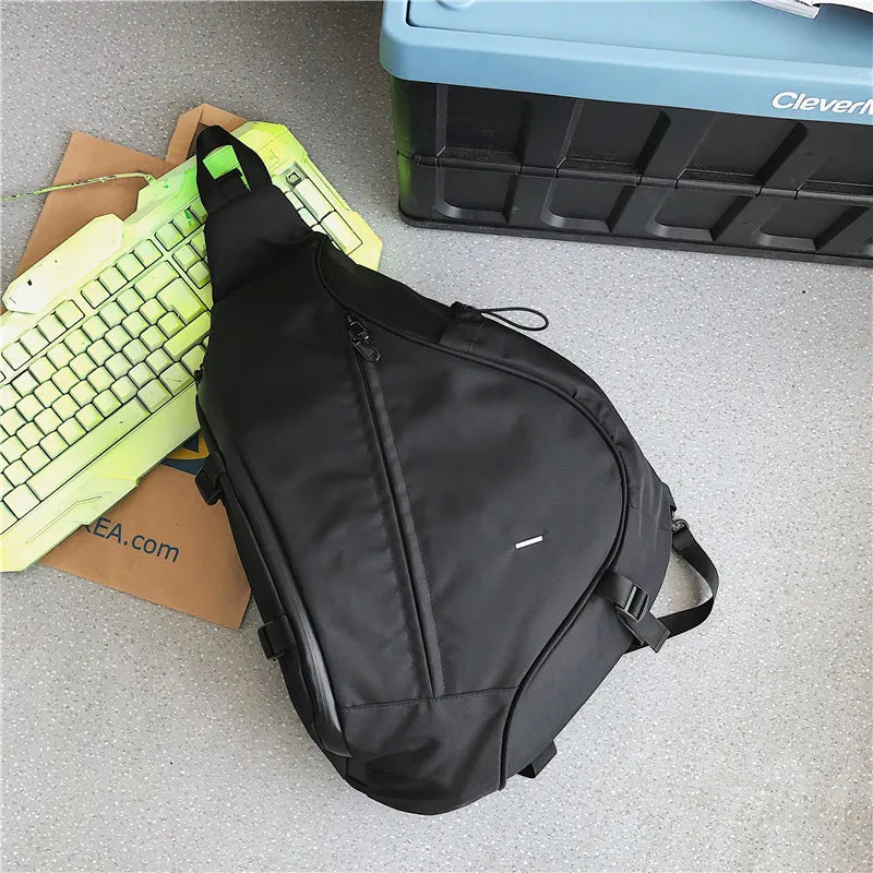 Black sling bag on a gray surface with a keyboard and storage box in the background.