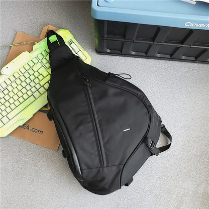Black sling bag on a gray surface with a keyboard and storage box in the background.