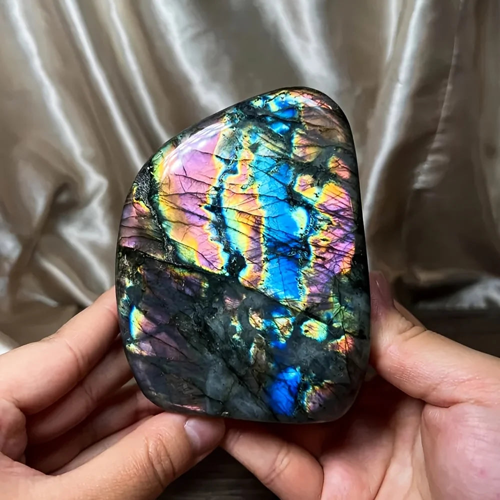 Multicolored labradorite stone held between two hands against a neutral background