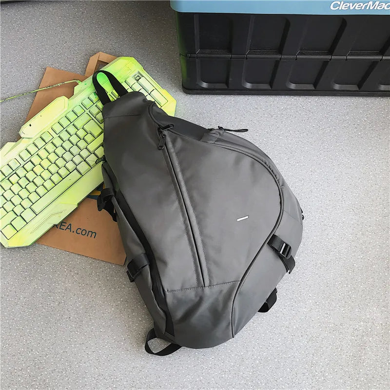 Gray sling bag on a gray floor with a green keyboard and brown box in the background.
