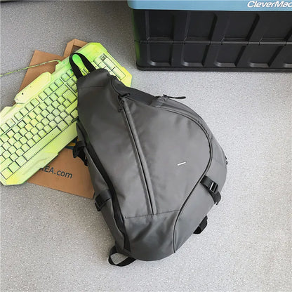 Gray sling bag on a gray floor with a green keyboard and brown box in the background.