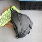 Gray sling bag on a gray floor with a green keyboard and brown box in the background.