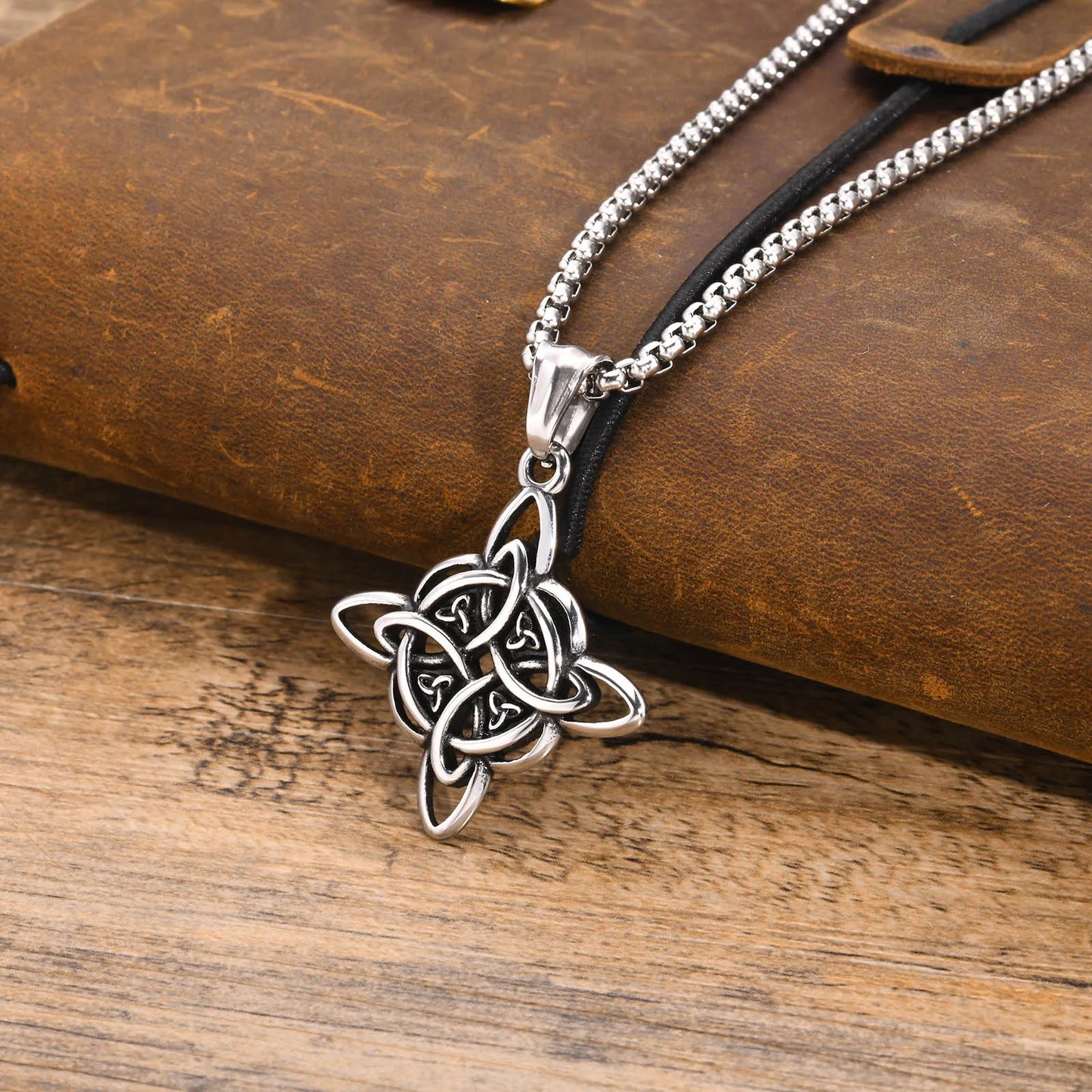 Vnox stainless steel Celtic witches knot pendant on a box chain, displayed over a vintage leather journal.