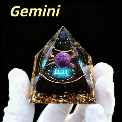 Pyramid-shaped object with astrological design labeled 'Gemini' held by a gloved hand against a black background.