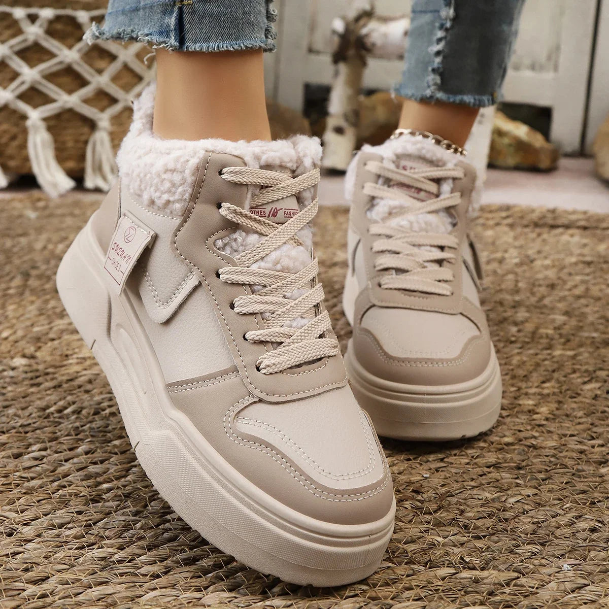 Beige high-top sneakers with white soles on a textured floor.