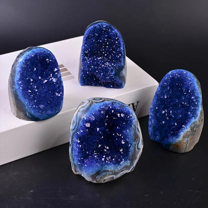 Four blue geode-like rocks on a black surface with a white box in the background.