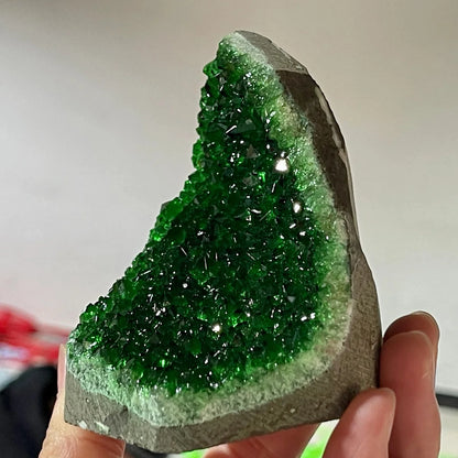 Green crystal rock held by a hand against a neutral background