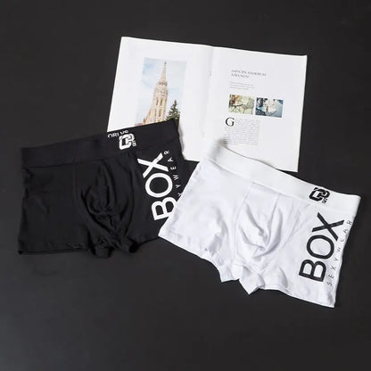 Black and white boxer briefs with 'BOX' branding on a dark surface with a newspaper.